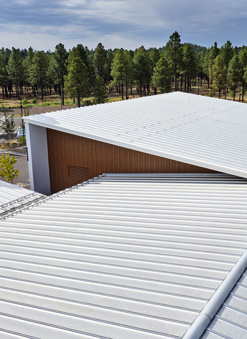 White standing-seam metal roof planes meeting at a valley with wood accent wall panels 
